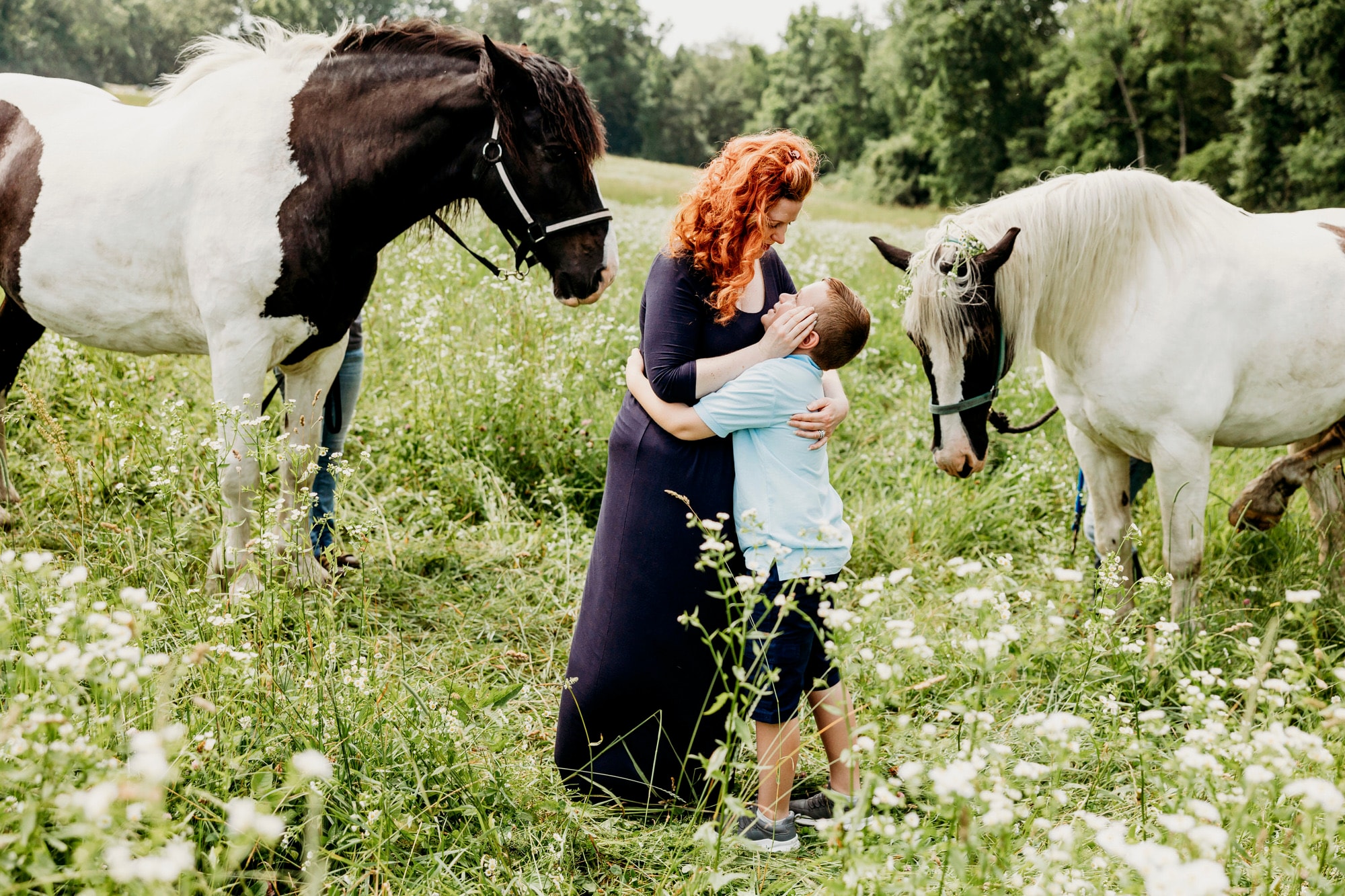 Woman holding child surrounded by horses in the pasture